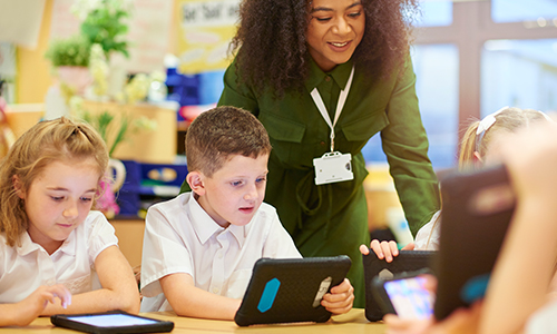 Teacher overlooking primary school student using mobile windows device