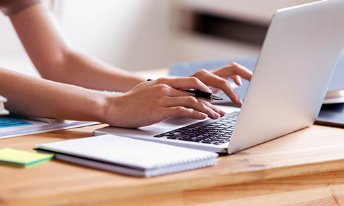Male student in iniform using laptop device in classroom