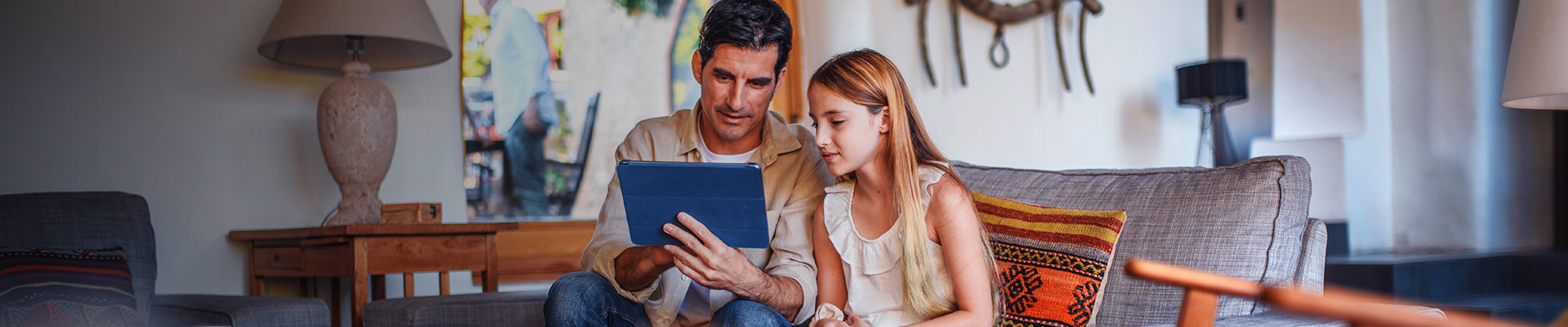 Male parent using mobile device with his daughter at home
