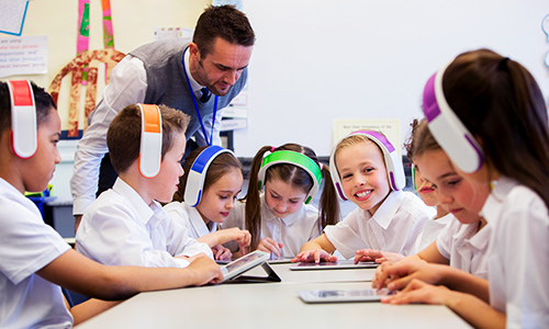 Teacher overlooking students using tablets and headsets in classroom