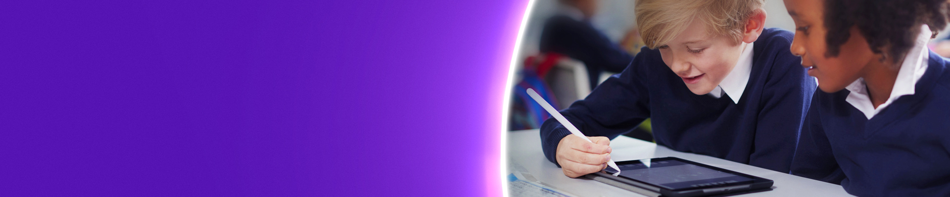School pupils sat at a desk in a classroom using a device
